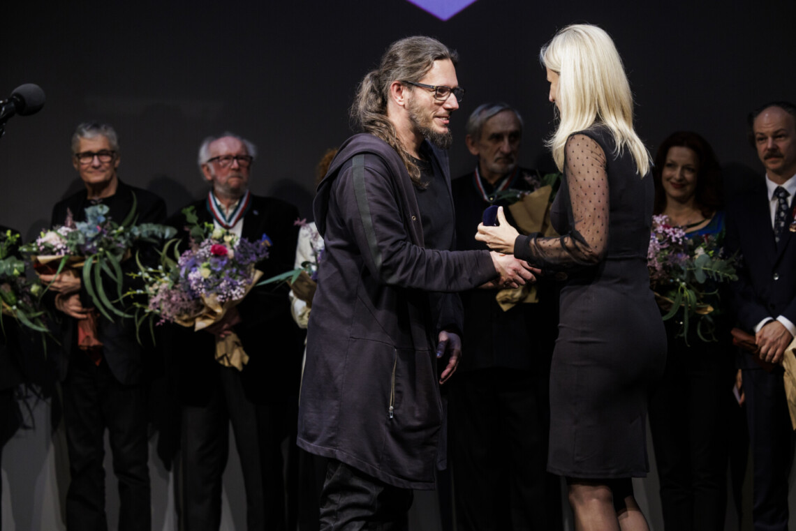 Przemysław Jędroska odbiera odznakę z rąk Radnej Aleksandry Poloczek. W tle stoją pozostałe nagrodzone osoby.
