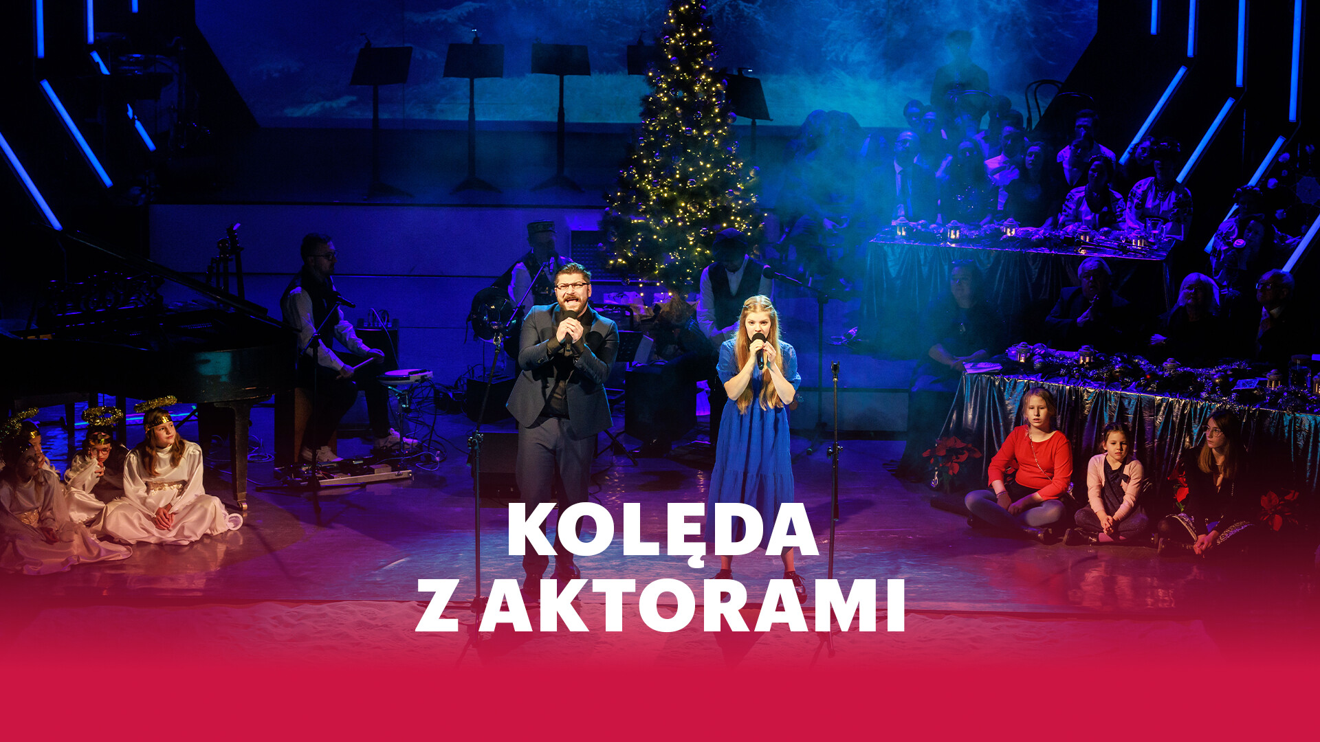 Grafika: w centrum kobieta i mężczyzna śpiewający do mikrofonu, za nimi zespół muzyczny oraz świecąca choinka, z prawej strony ustawione są stoły, za którymi siedzą ludzie, przed pierwszym stołem na podłodze siedzą dwie dziewczynki, w dole grafiki na czerwonym tle biały napis: Kolęda z aktorami