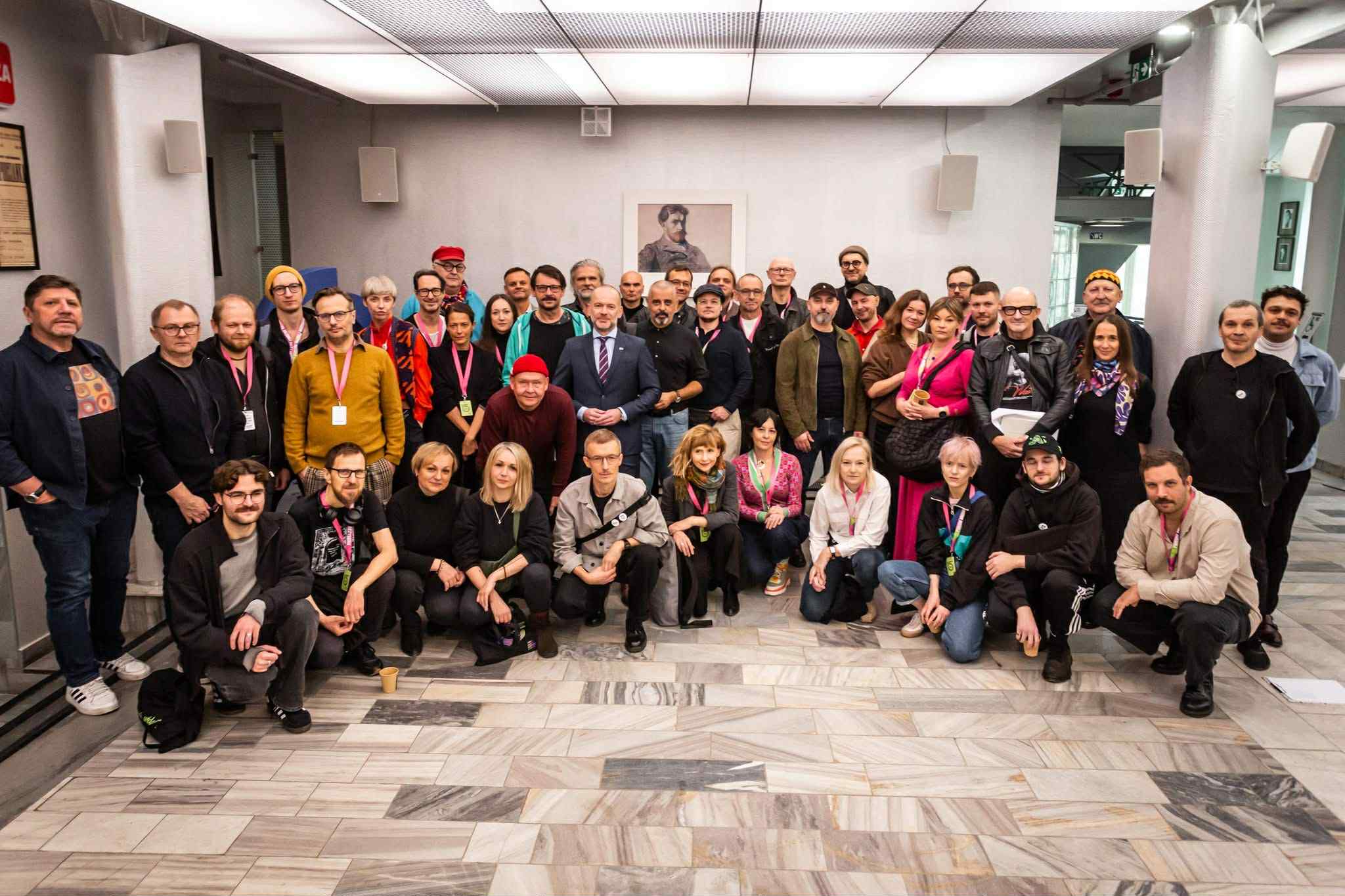 Grupa ludzi pozuje do zdjęcia. Część osób kuca, większość stoi w półkole.