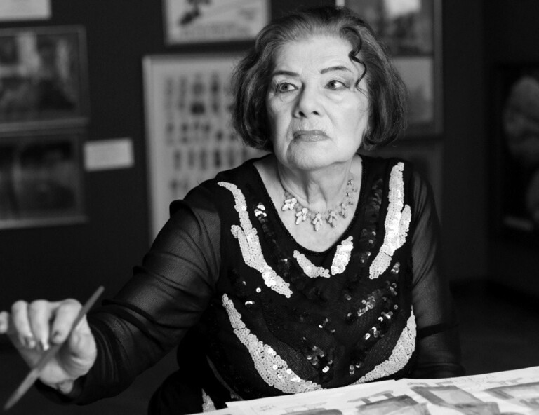 Zdjęcie kobiety za stołem, w prawej dłoni trzyma pędzel, patrzy w bok, zdjęcie czarno-białe