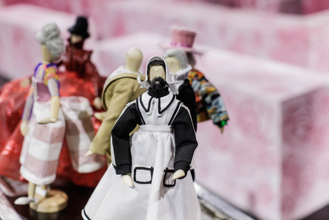 Drewniane, małe manekiny z kostiumami ze spektaklu Alicja w Krainie Czarów, na pierwszym planie Kucharka w białym fartuchu