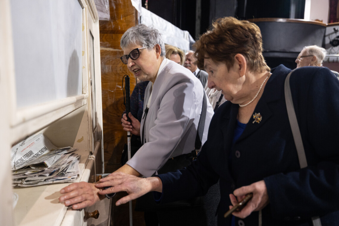 Osoby dotykające jasnego kredensu stanowiącego scenografię spektaklu Byk