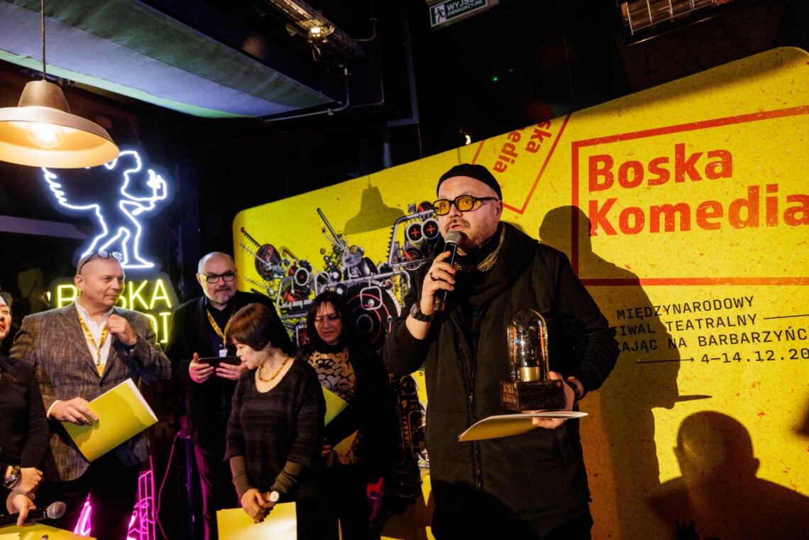 Marcin Gaweł przemawia do mikrofonu, w lewej dłoni trzyma nagrodę