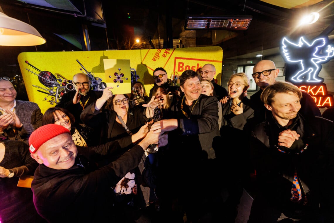 Grupa ludzi z Teatru stojących razem, kilka osób trzyma razem nagrodę, wszyscy są uśmiechnięci