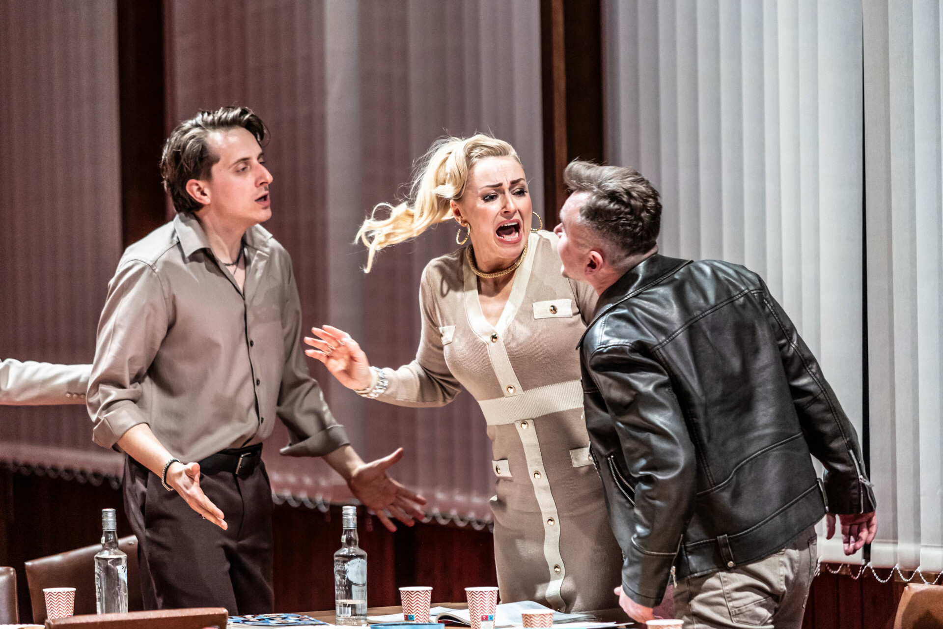 Dwóch mężczyzn oraz kobieta w trakcie kłótni, uchwyceni w ruchu, kobieta ma otwarte usta i włosy w kucyku rozwiane na bok