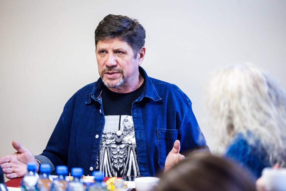 Dyrektor Robert Talarczyk siedzący za stołem, dłonie ma rozłożone, oparte bokiem na stole