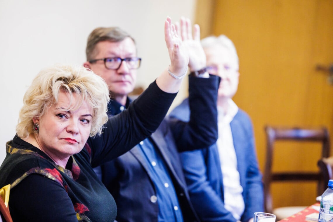 Przy osoby przy stole, dwie z nich podnoszą rękę w górę