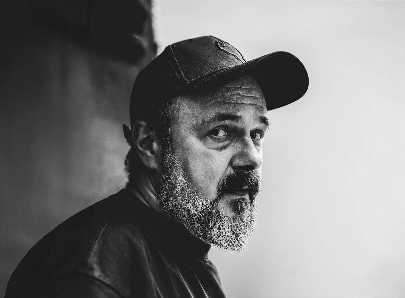 Czarno-białe zdjęcie Arkadiusza Jakubika z profilu, mężczyzna z brodą w czapce z daszkiem