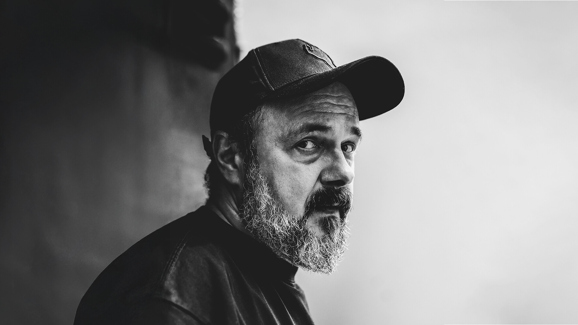 Czarno-białe zdjęcie Arkadiusza Jakubika z profilu, mężczyzna z brodą w czapce z daszkiem